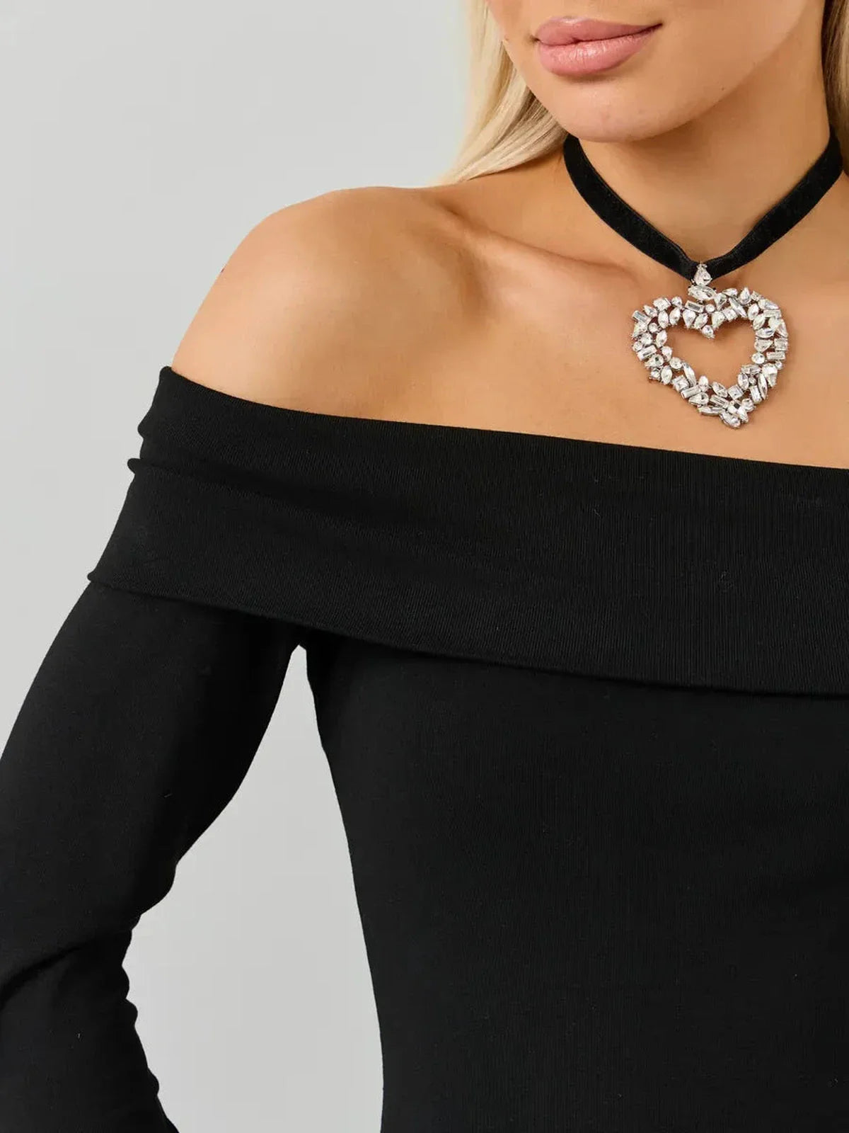 Close-up of a woman wearing an off-the-shoulder black dress with a heart-shaped jeweled necklace.