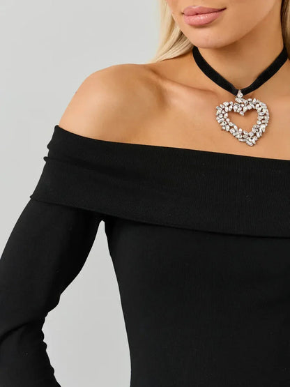 Close-up of a woman wearing an off-the-shoulder black dress with a heart-shaped jeweled necklace.