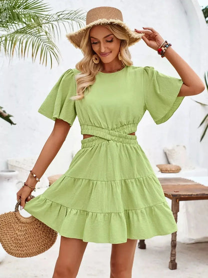 Model in a chic green Palm Bloom Mini Dress with flutter sleeves and tiered skirt, perfect for summer occasions.