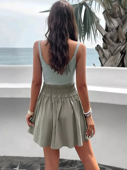 Model wearing a mint-sage Palm Haze Mini Dress with a flared skirt by the beach, showcasing a stylish summer look.