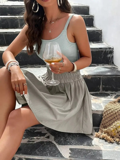 Stylish woman in a mint-sage mini dress enjoying a drink on outdoor steps, perfect for summer outings.