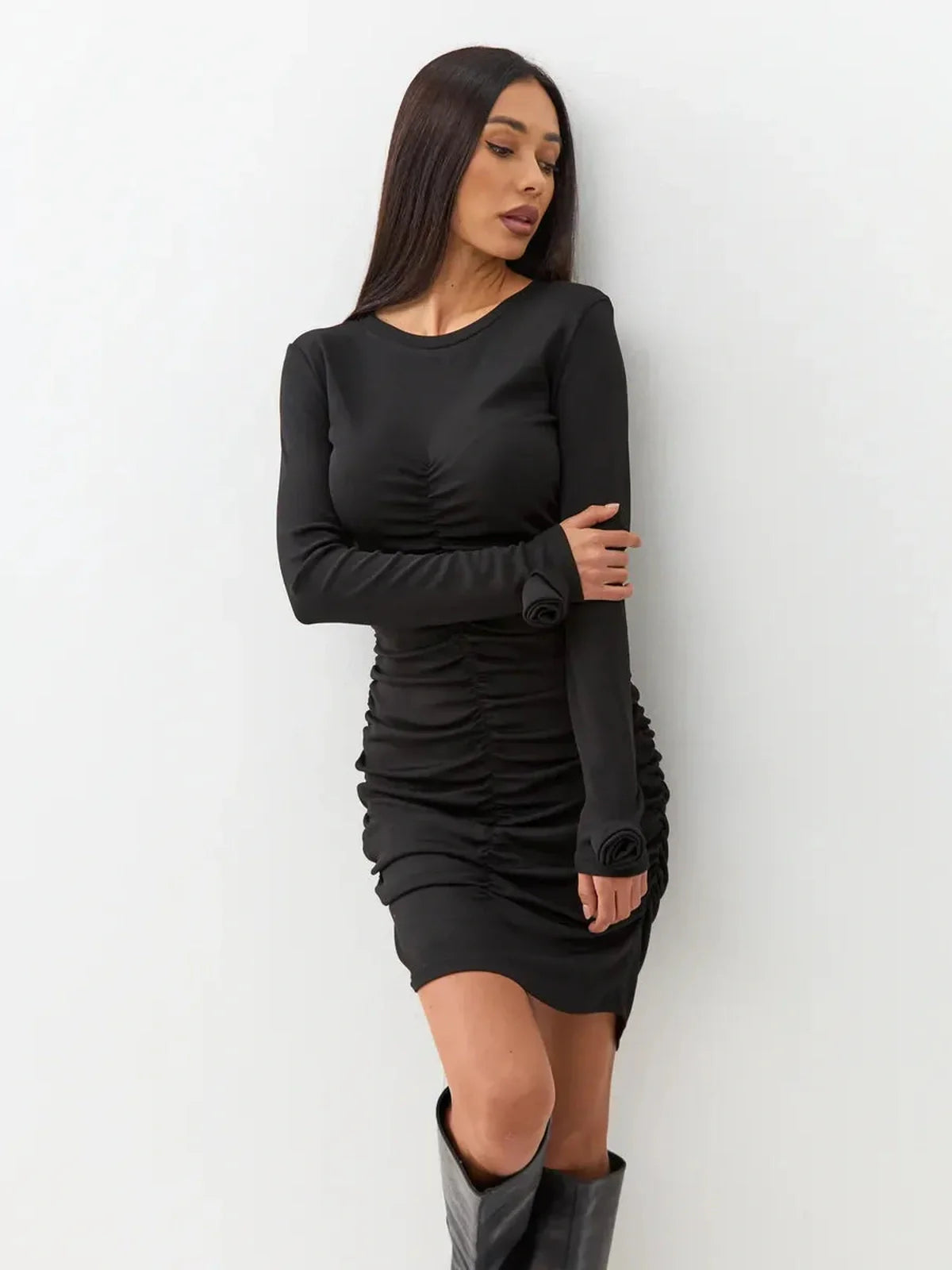 Model wearing a form-fitting black mini dress with long sleeves and gathered ruching, perfect for evening elegance.