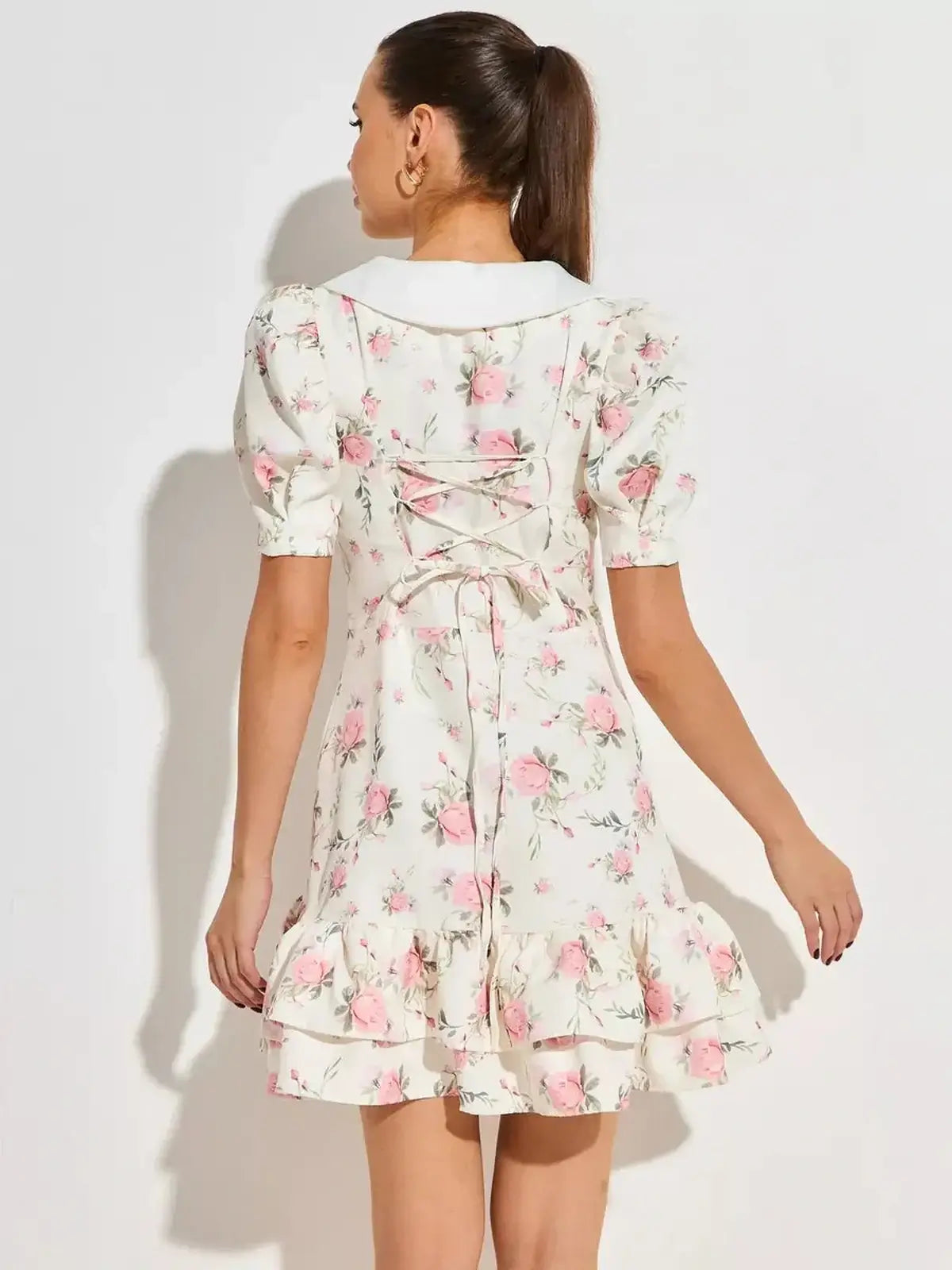 Back view of a feminine floral mini dress with puffed sleeves and flared hem, featuring pink roses on a white background.