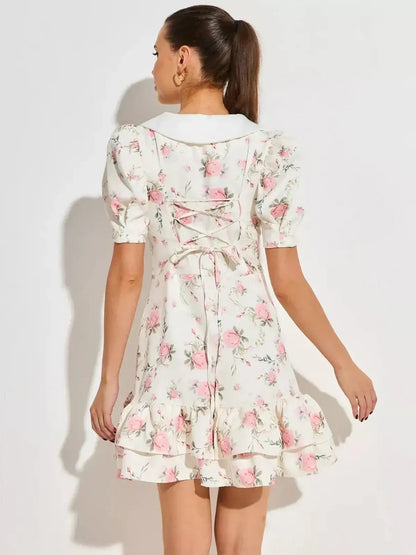 Back view of a feminine floral mini dress with puffed sleeves and flared hem, featuring pink roses on a white background.