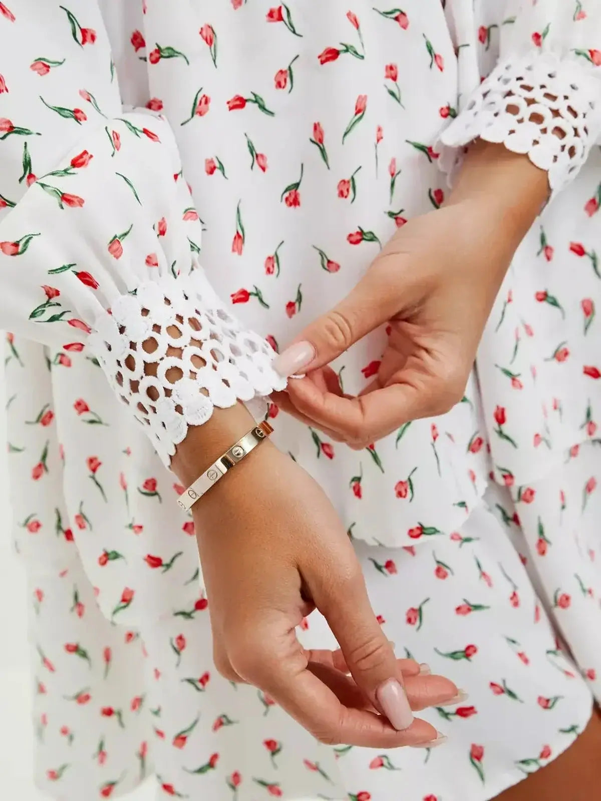 Detail of a woman adjusting the cuff of a white mini dress with rosebud print and lace trim, perfect for summer celebrations.