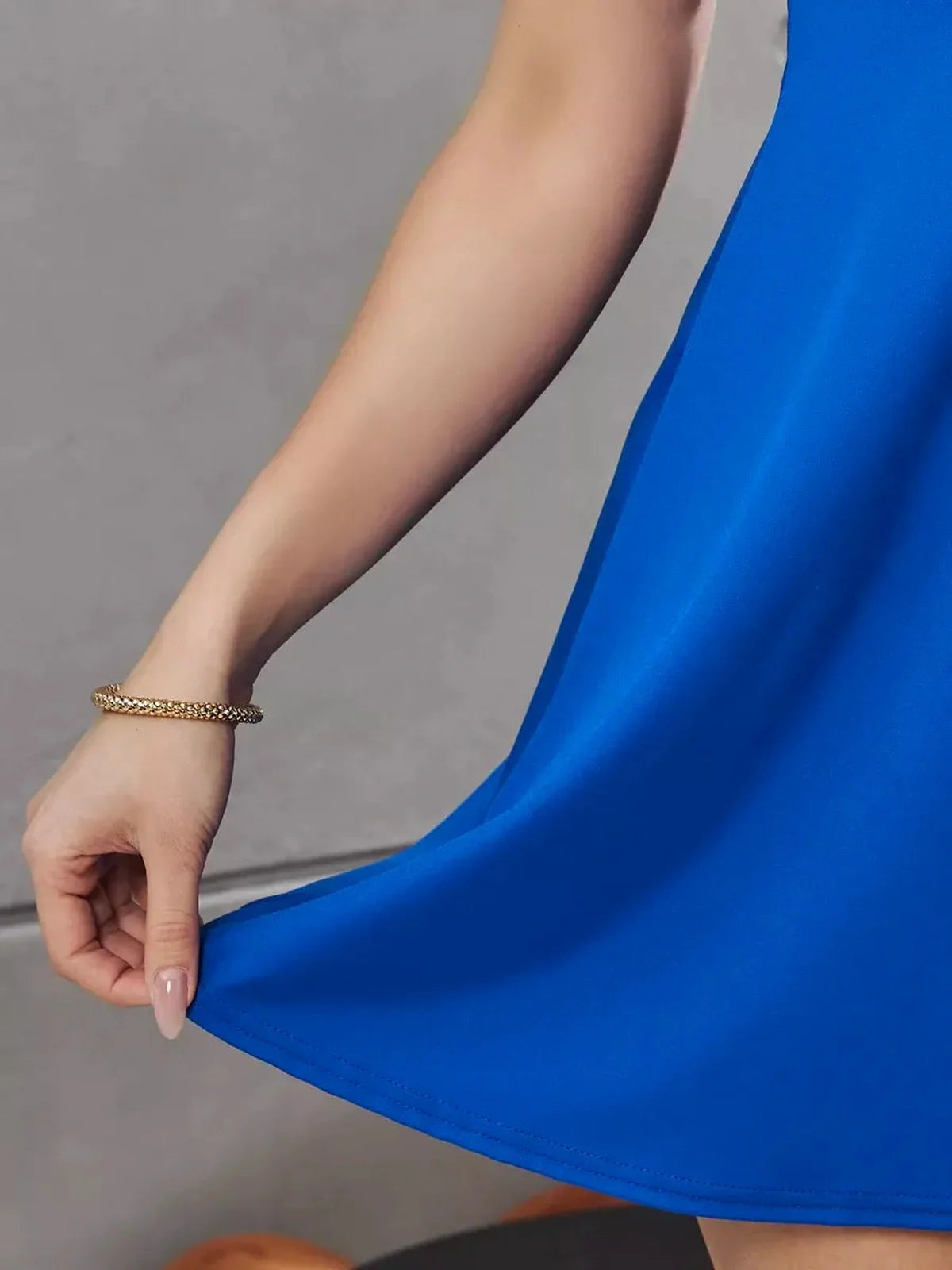 Close-up of a model's hand lightly grasping the hem of a blue Royal Twist Mini Dress, showcasing its flowy fabric.
