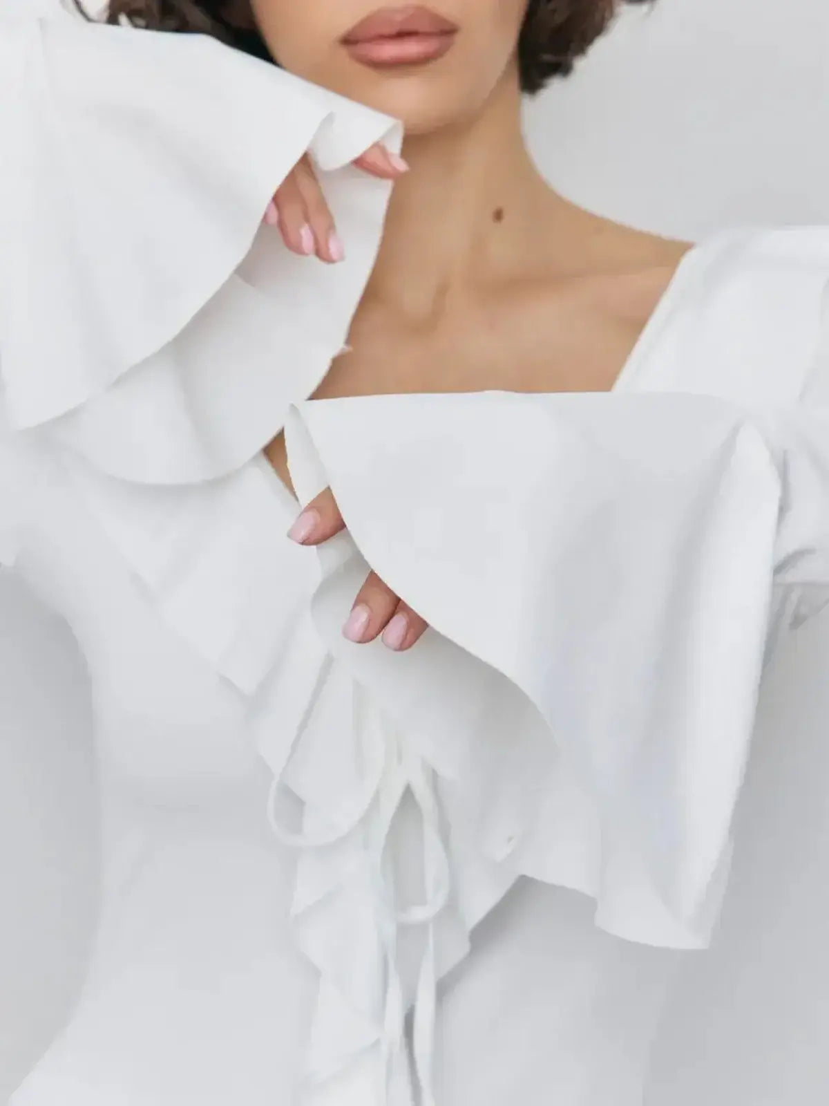 Close-up of a woman wearing a white mini dress with flowing ruffle sleeves and a deep V-neckline.