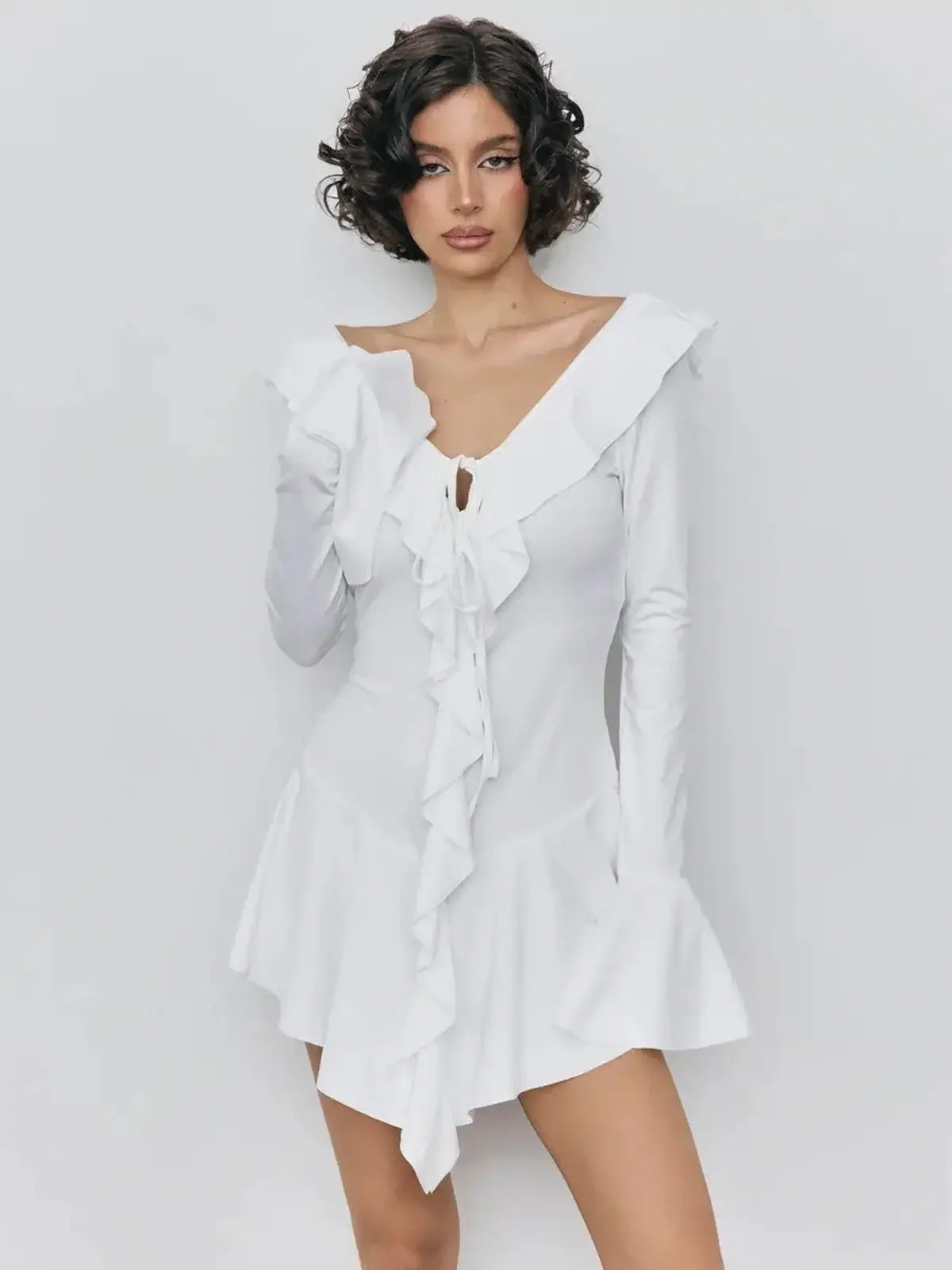 Model wearing a white mini dress with cascading ruffles and deep V-neckline, perfect for summer or special occasions.