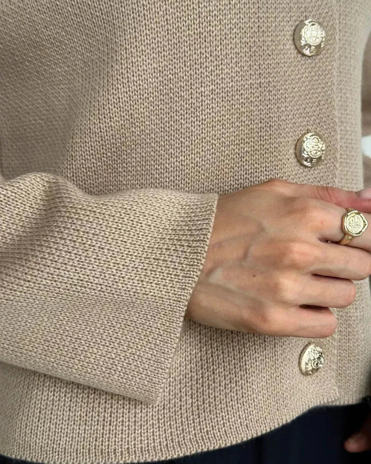 Close-up of a hand wearing a ring and buttoned Sable Cardigan by Slimona in elegant beige knit.