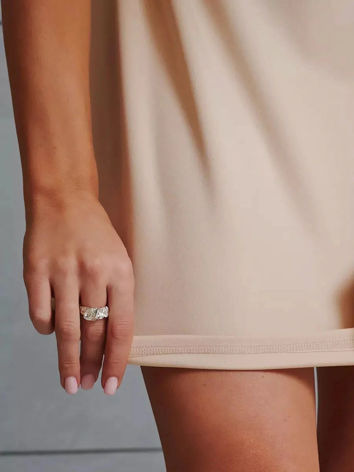 Close-up of a hand wearing a silver ring, showcasing the hem of a beige satin mini dress.
