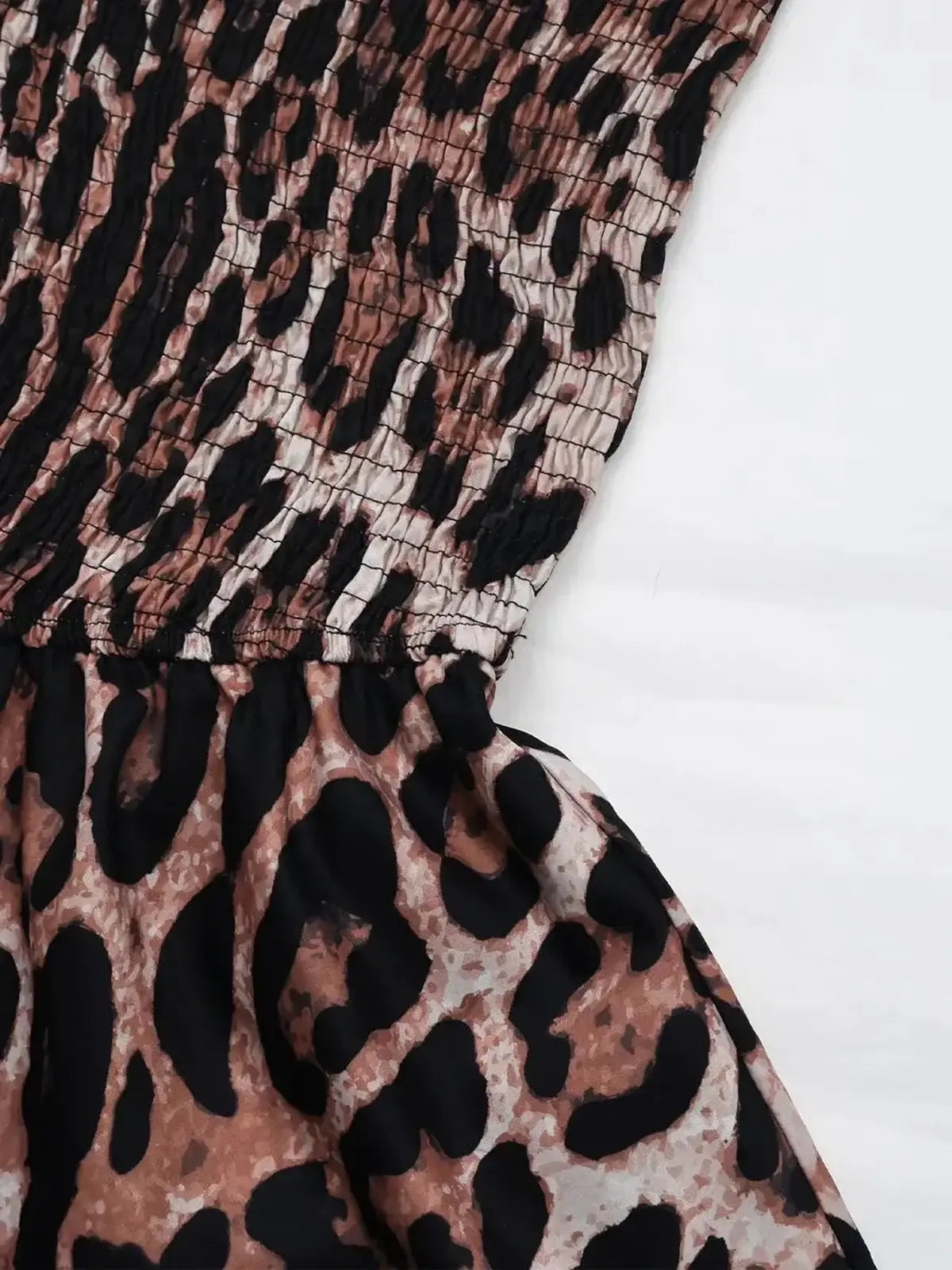 Close-up of the smocked bodice and ruffle skirt of a leopard print mini dress, showcasing playful summer fashion.