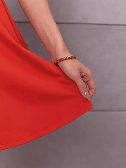 Close-up of a hand holding the hem of a vibrant red mini dress, showcasing its stylish flair.