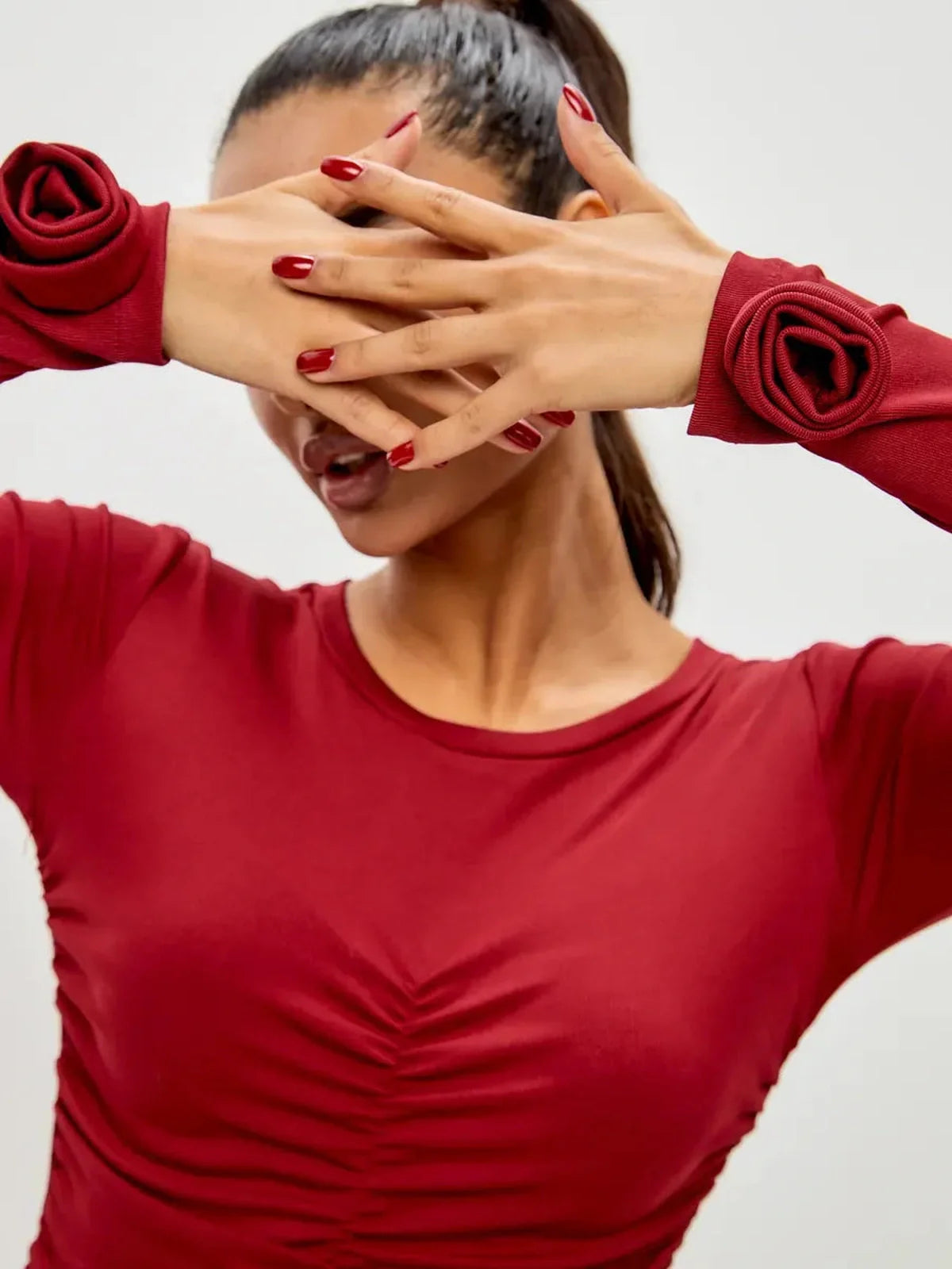 Model showcasing a ruched burgundy dress with rose details on long sleeves, perfect for party and cocktail occasions.