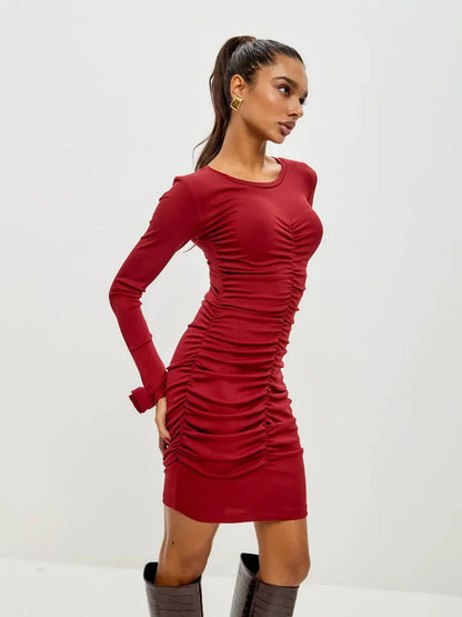 Model wearing a red ruched mini dress with long sleeves, showcasing a body-hugging silhouette for party occasions.