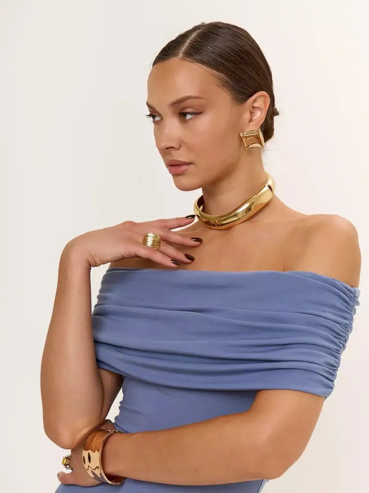 Woman in a blue off-shoulder dress with gold accessories, showcasing elegance and modern design.