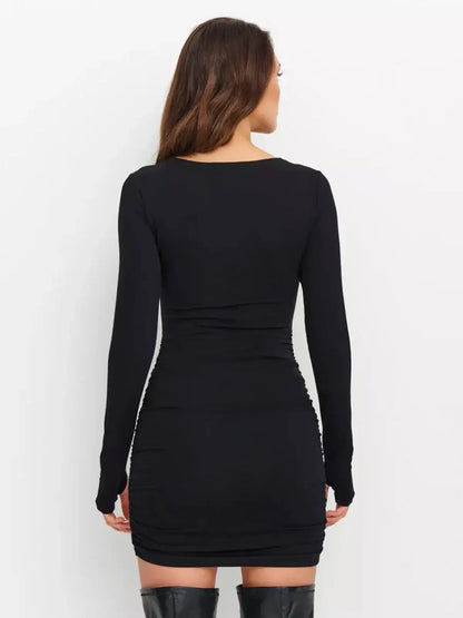Model showcasing the back view of a Sculpted Hour Mini Dress in black, featuring long sleeves and a ruched design.