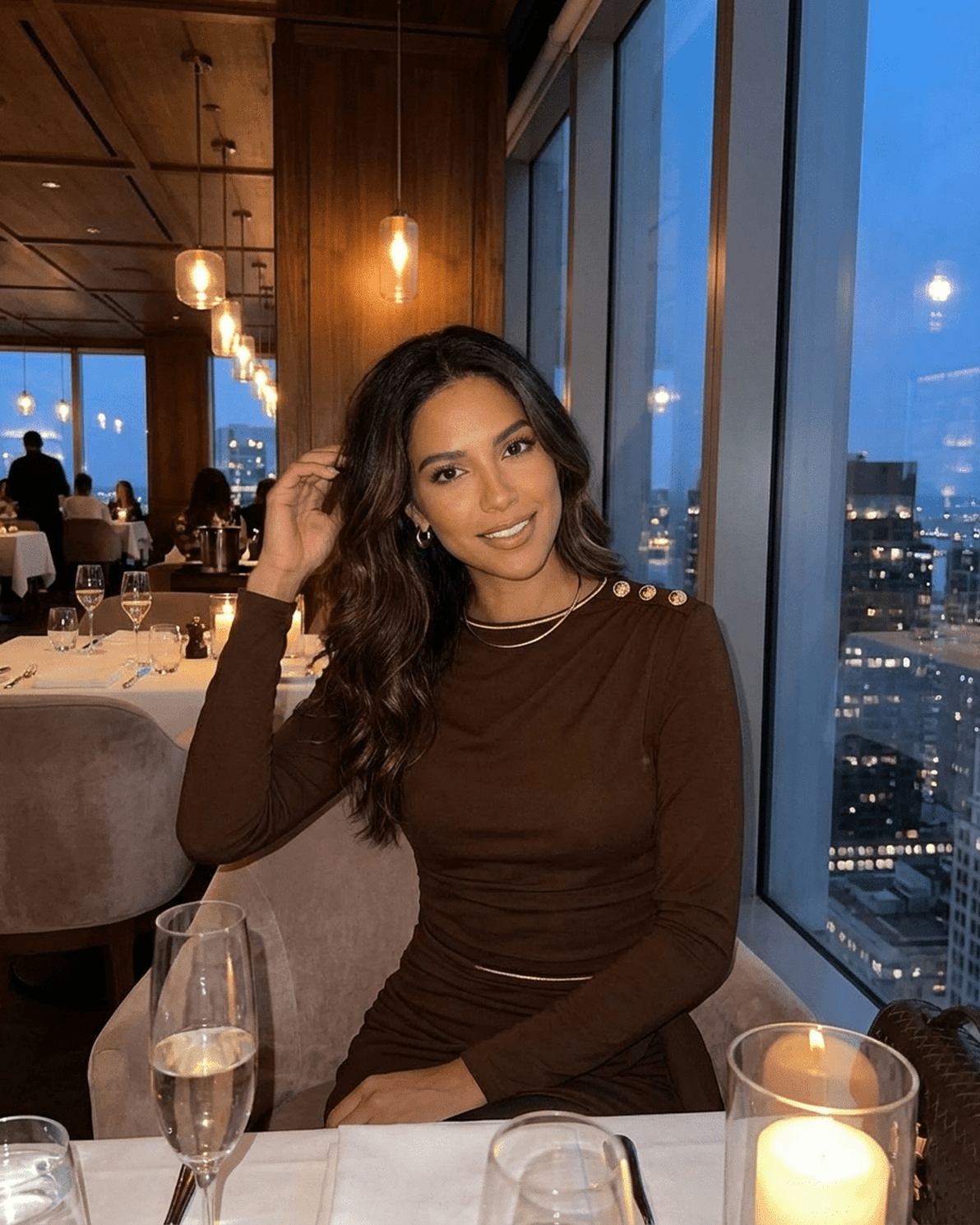 Model wearing Sienna Mini Dress by Slimona in a stylish restaurant setting with city views.