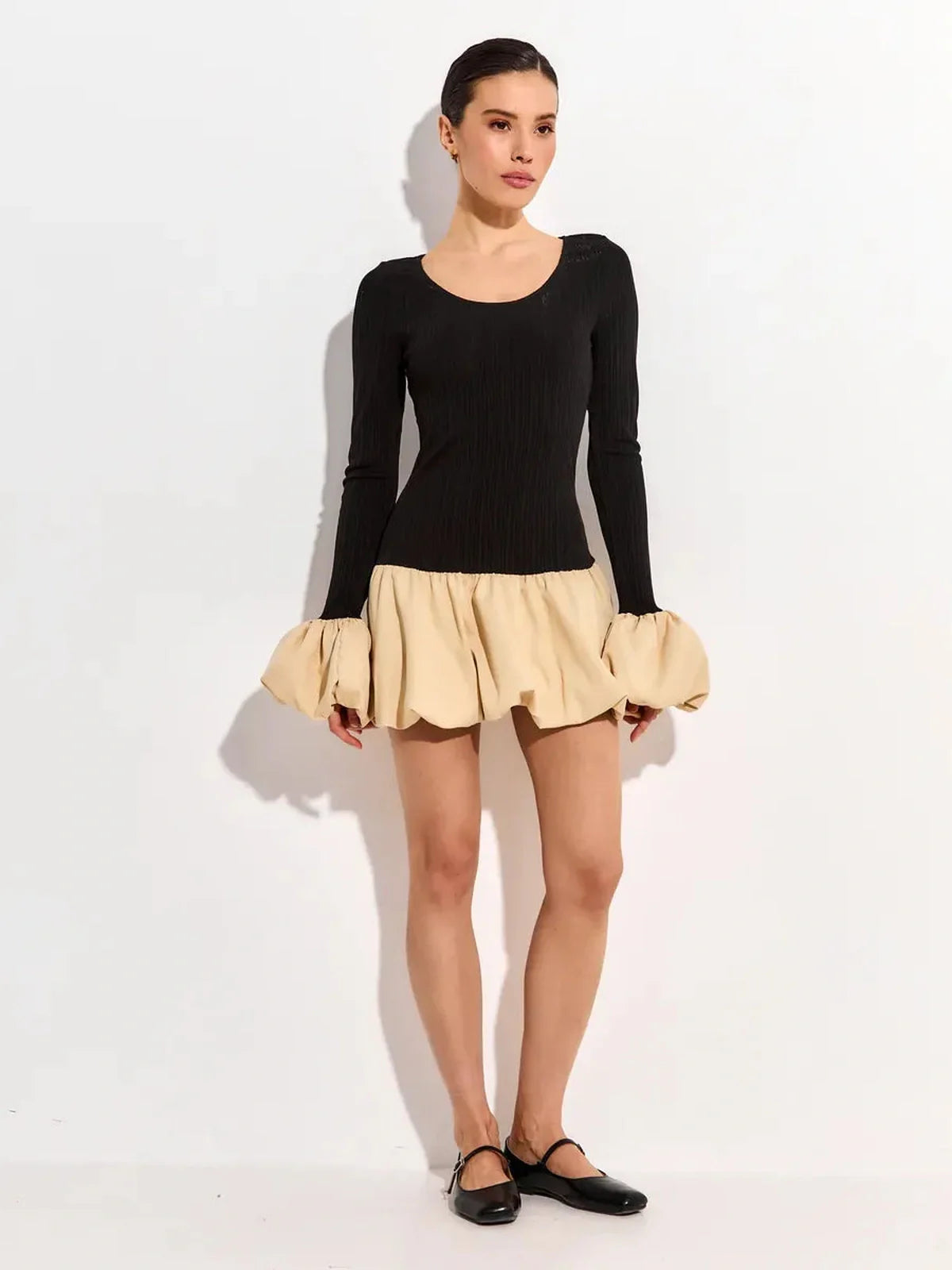 Model showcasing the Split Statement mini dress with long sleeves, featuring a black ribbed top and a beige voluminous skirt.
