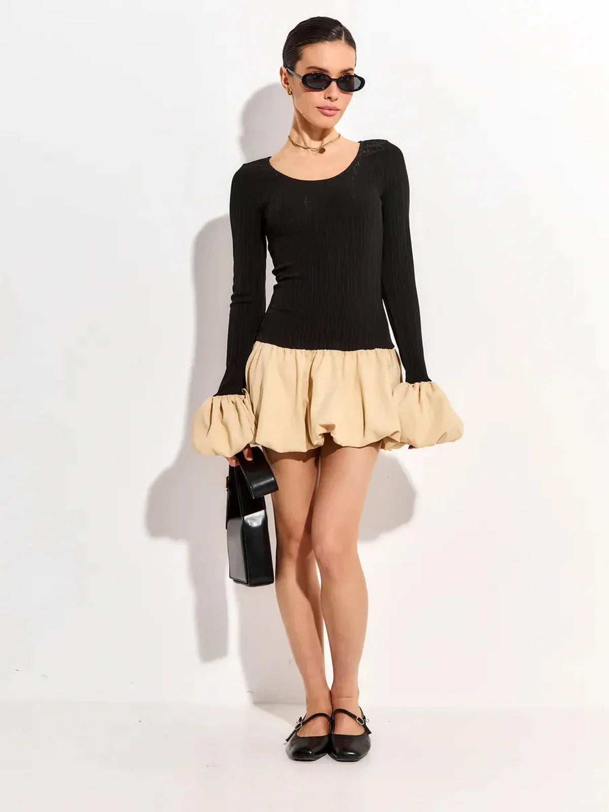 Model in a black long sleeve top and beige bubble mini dress with sunglasses and a stylish handbag.