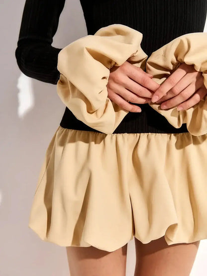 Model showcasing the Split Statement mini dress with bold bubble skirt and halter neckline in soft beige and black.