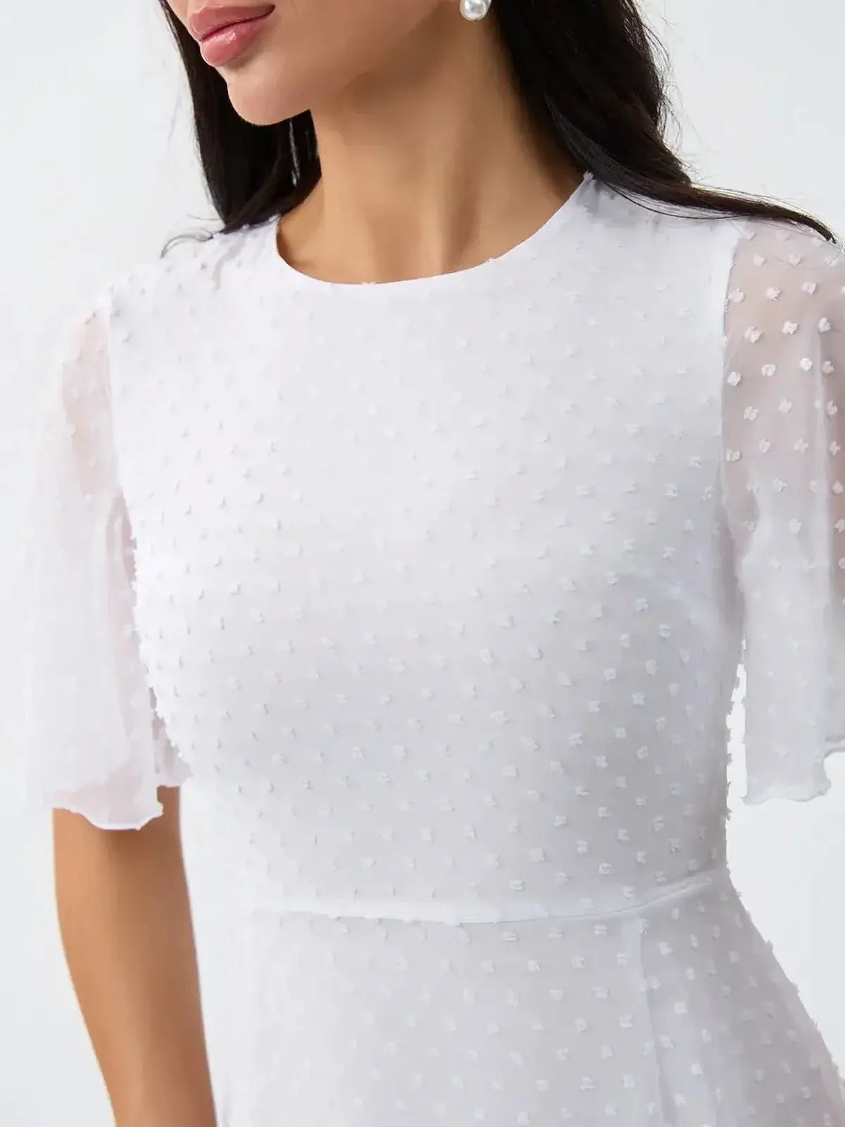 Close-up of a woman in a white ruffle mini dress with sheer polka-dot sleeves, perfect for summer or wedding events.