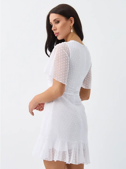 Model wearing the Starlight Ruffle Mini white dress with textured polka dots and flouncy hem.