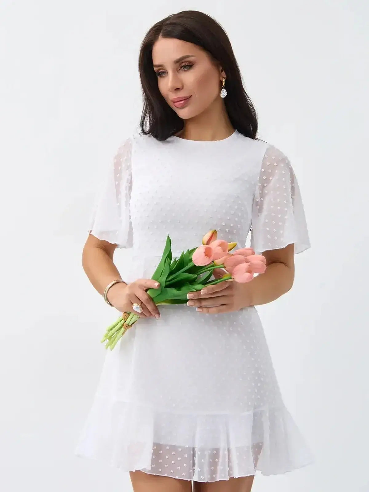 Model wearing a Starlight Ruffle Mini white dress with polka dots, holding tulips, perfect for summer and wedding guest occasions.