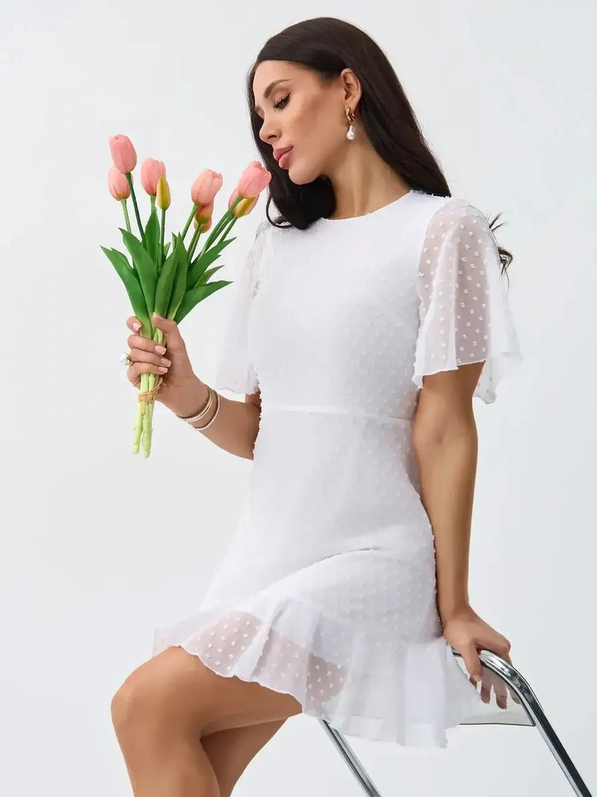 Model showcasing the Starlight Ruffle Mini white dress with polka-dot texture, holding tulips, exuding elegance.
