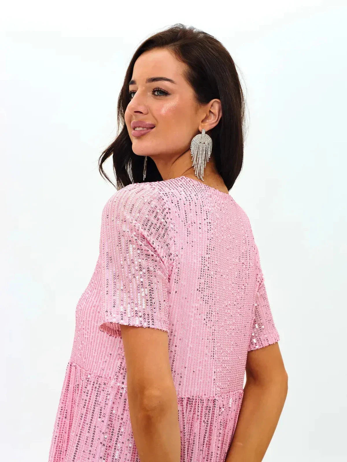 Back view of a woman wearing a pink sequin mini dress, showcasing a flirty A-line silhouette and elegant earrings.