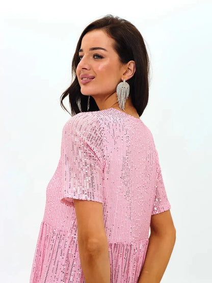 Back view of a woman wearing a pink sequin mini dress, showcasing a flirty A-line silhouette and elegant earrings.