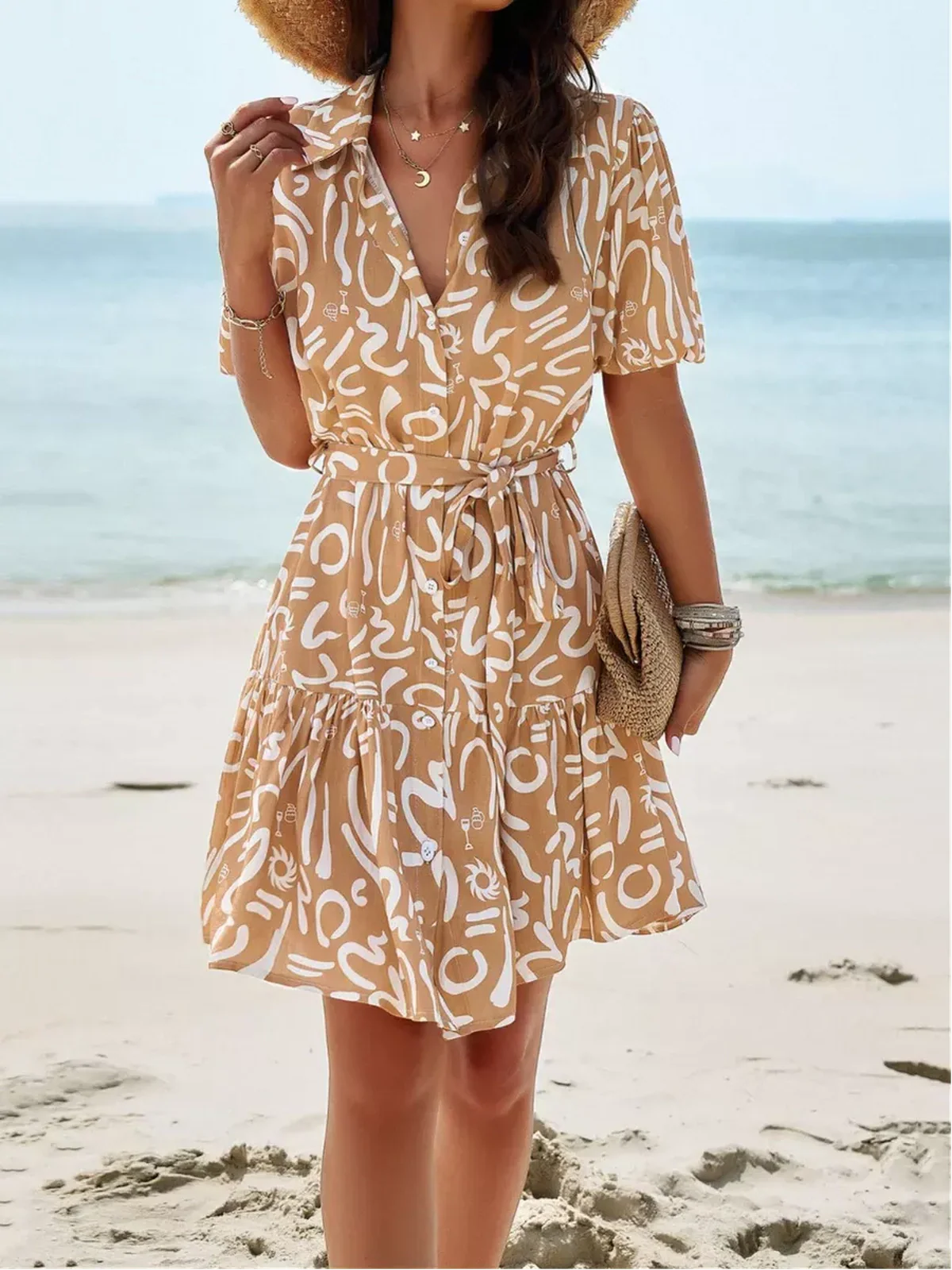 Model wearing the Sunstroke Mini Dress on the beach, featuring a stylish pattern and self-tie waist.