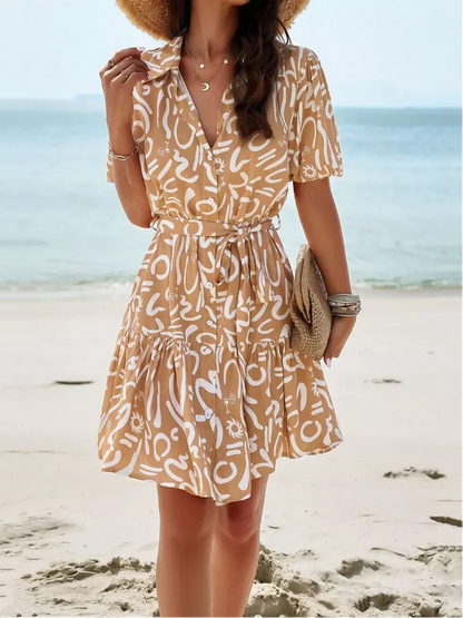 Model wearing the Sunstroke Mini Dress on the beach, featuring a stylish pattern and self-tie waist.