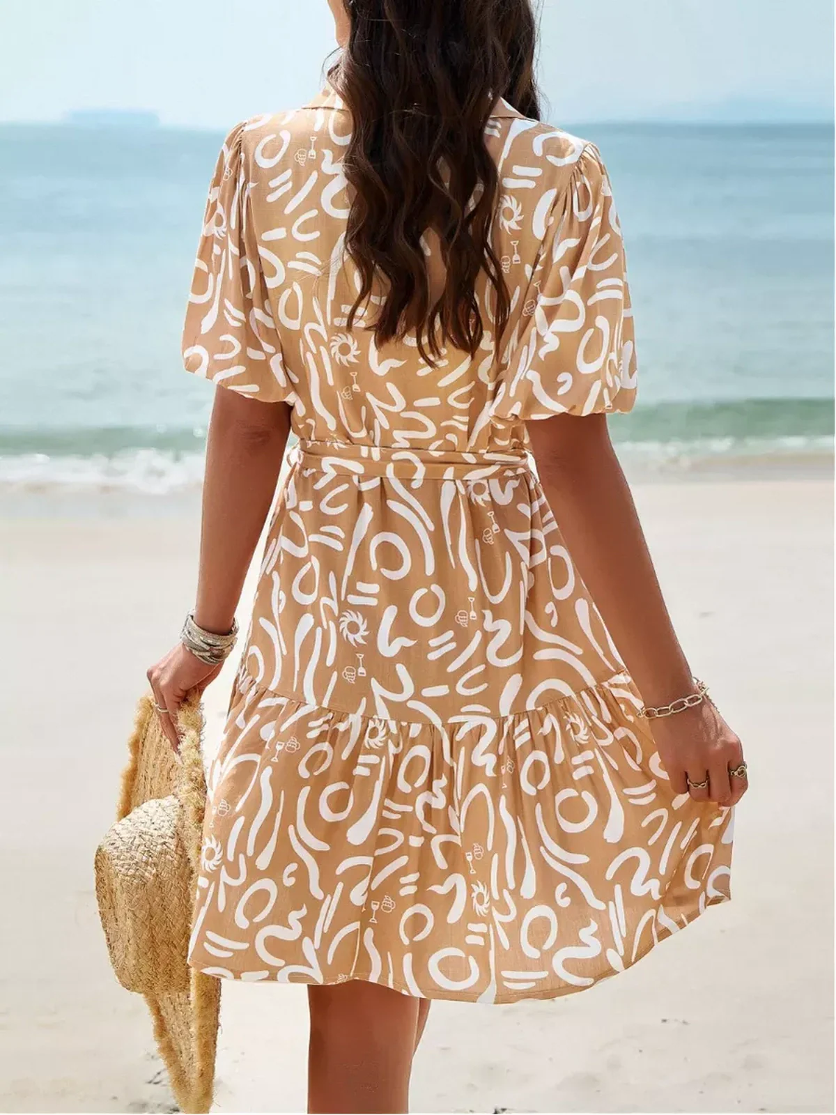 Model wearing a Sunstroke Mini Dress with abstract design at the beach, ideal for summer and wedding guests.