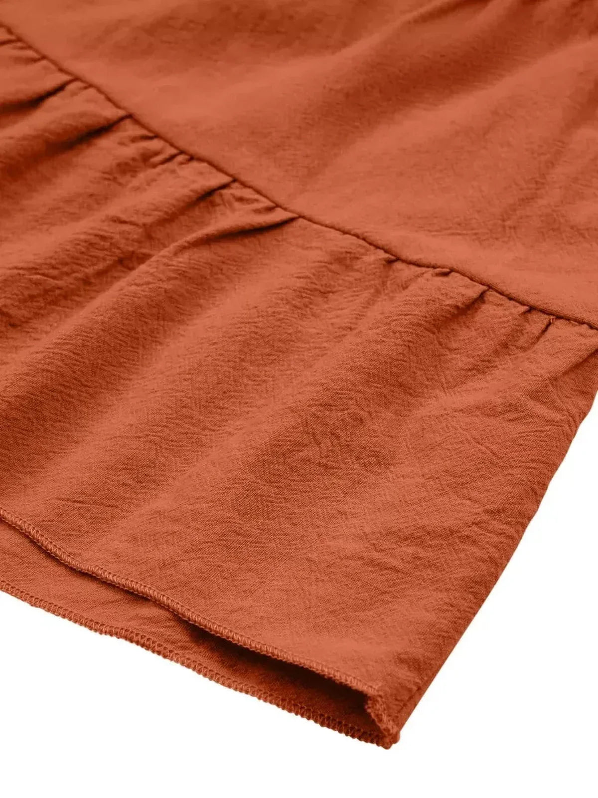 Close-up of the terracotta fabric of a mini dress featuring a textured finish and gathered detail.