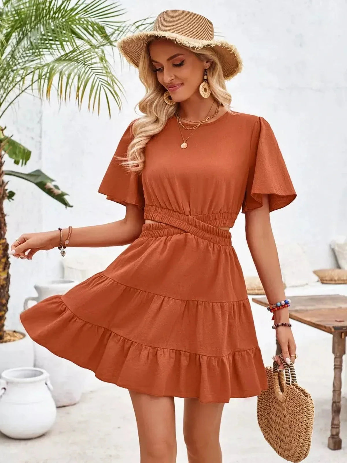 Woman in a terracotta flare mini dress with flutter sleeves, styled for summer outings and sunny weather.