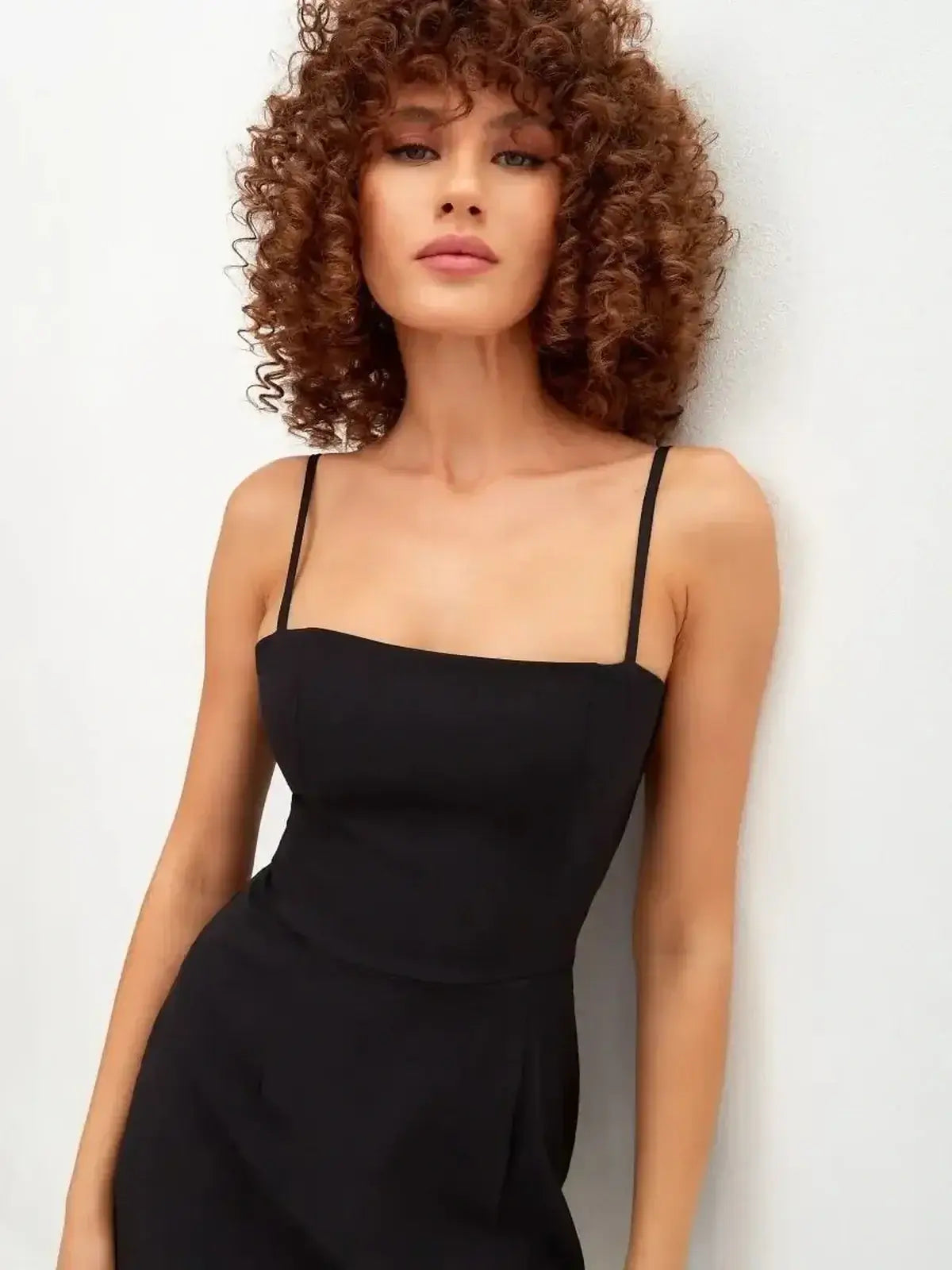 Model wearing a sleek black mini dress with adjustable straps and a minimalist square neckline.
