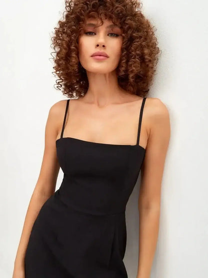 Model wearing a sleek black mini dress with adjustable straps and a minimalist square neckline.