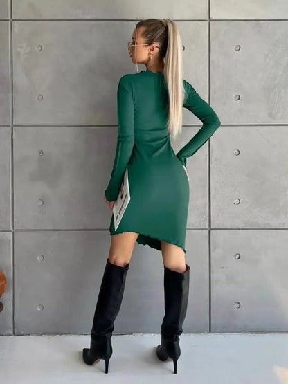 Fashion-forward model showcasing a long sleeve green mini dress with a stylish asymmetrical hem and sleek black knee-high boots.