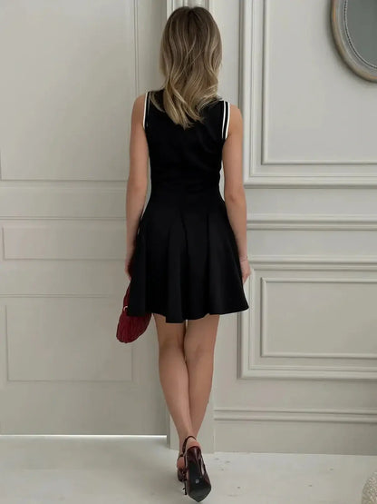 Back view of a woman in a sleeveless black varsity charm mini dress, featuring athletic stripes and a flared skirt.