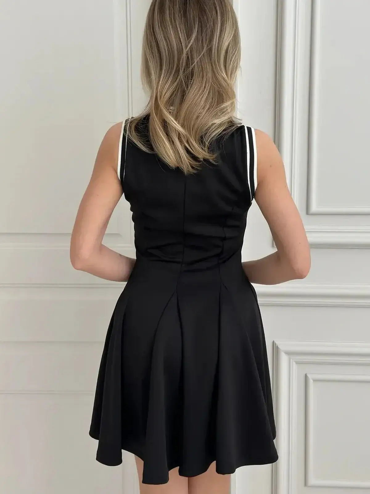 Back view of a black Varsity Charm Mini Dress with athletic stripes, showcasing a flattering fit and flared skirt.