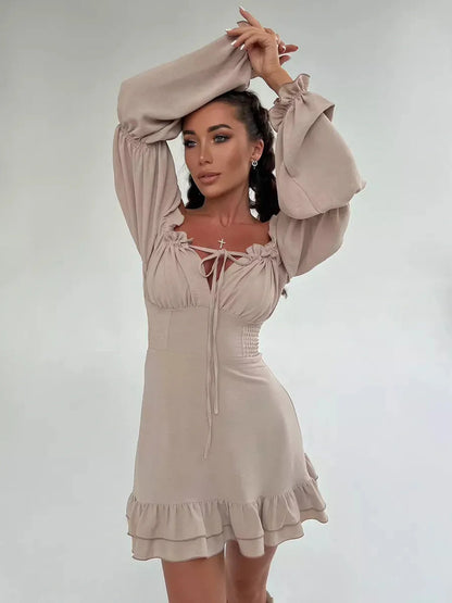 Woman in a beige Velina Ruffle Mini dress with off-shoulder design and puffed sleeves, perfect for summer parties.