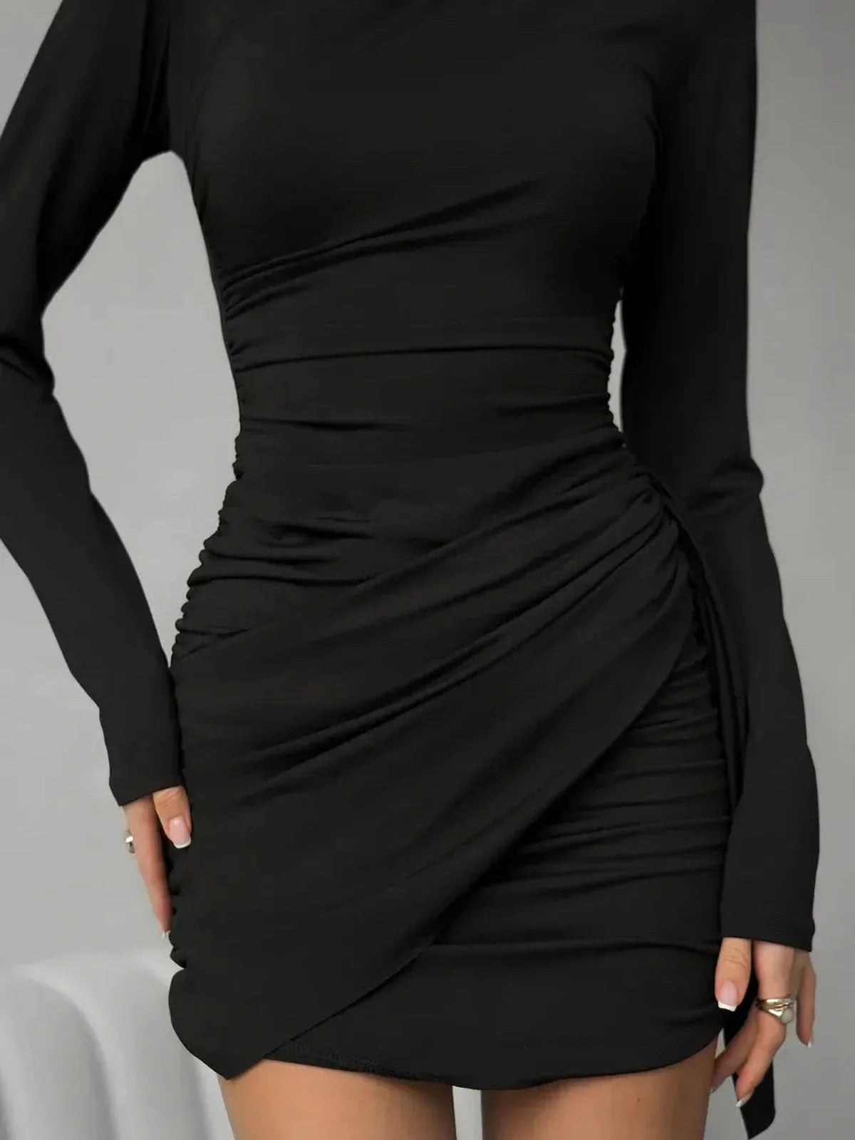Black mini dress with ruched detailing and long sleeves, perfect for cocktail parties and special occasions.
