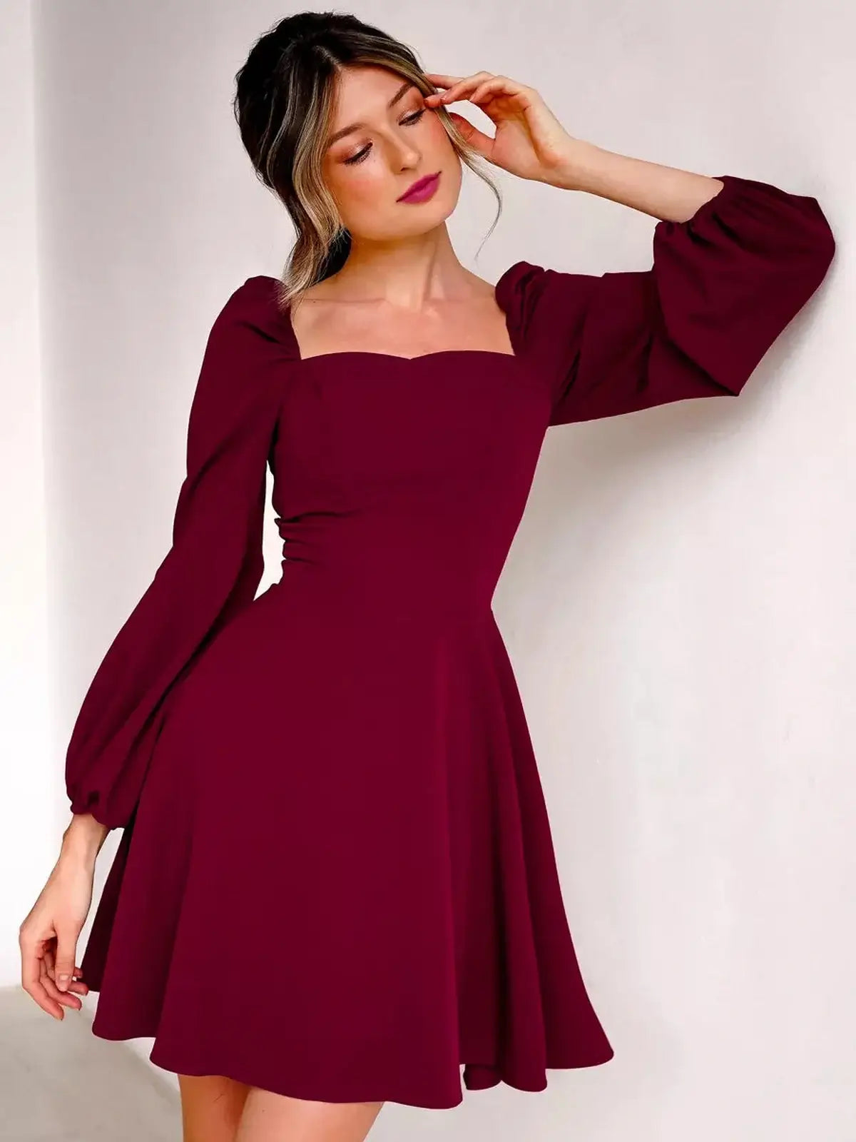 A model showcases a deep burgundy mini dress with a square neckline and voluminous long sleeves, exuding elegance.