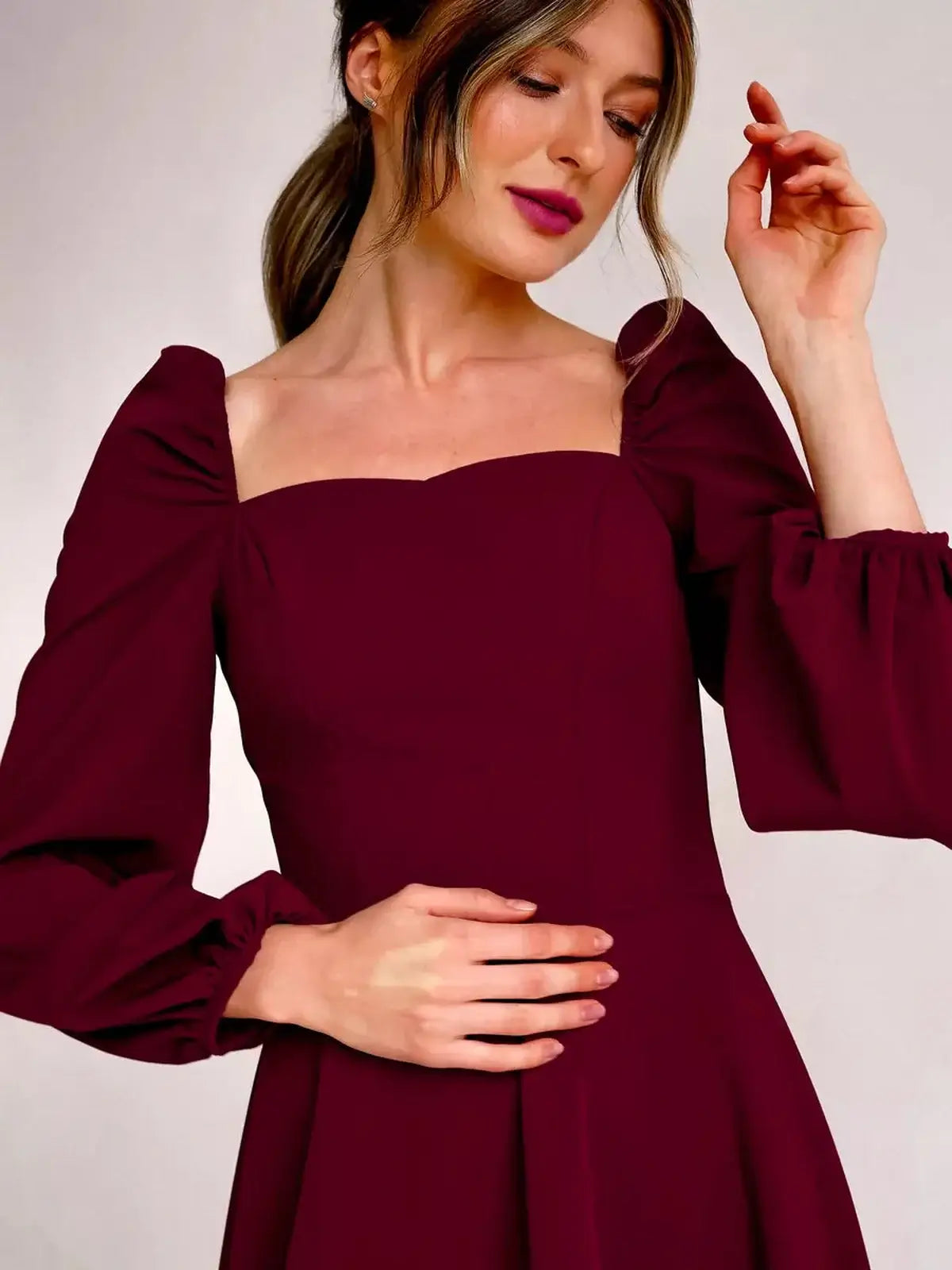 Model showcasing Velvet Ruby, a burgundy mini dress with a square neckline and voluminous long sleeves.