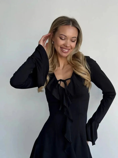 Model wearing a long sleeve black mini dress with a tie-front and ruffled details, exuding elegance and confidence.
