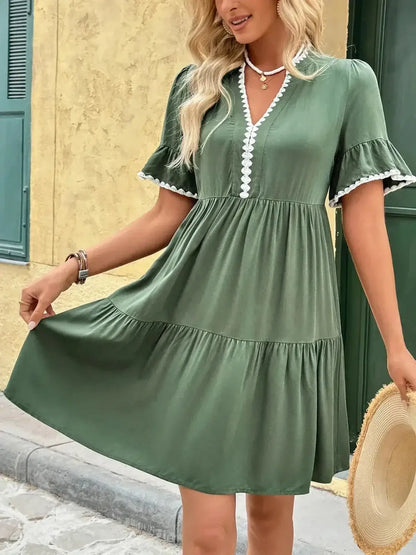 Model wearing the Veranda Bloom Mini Dress, a green summer dress with ruffle sleeves and white embroidered trim.