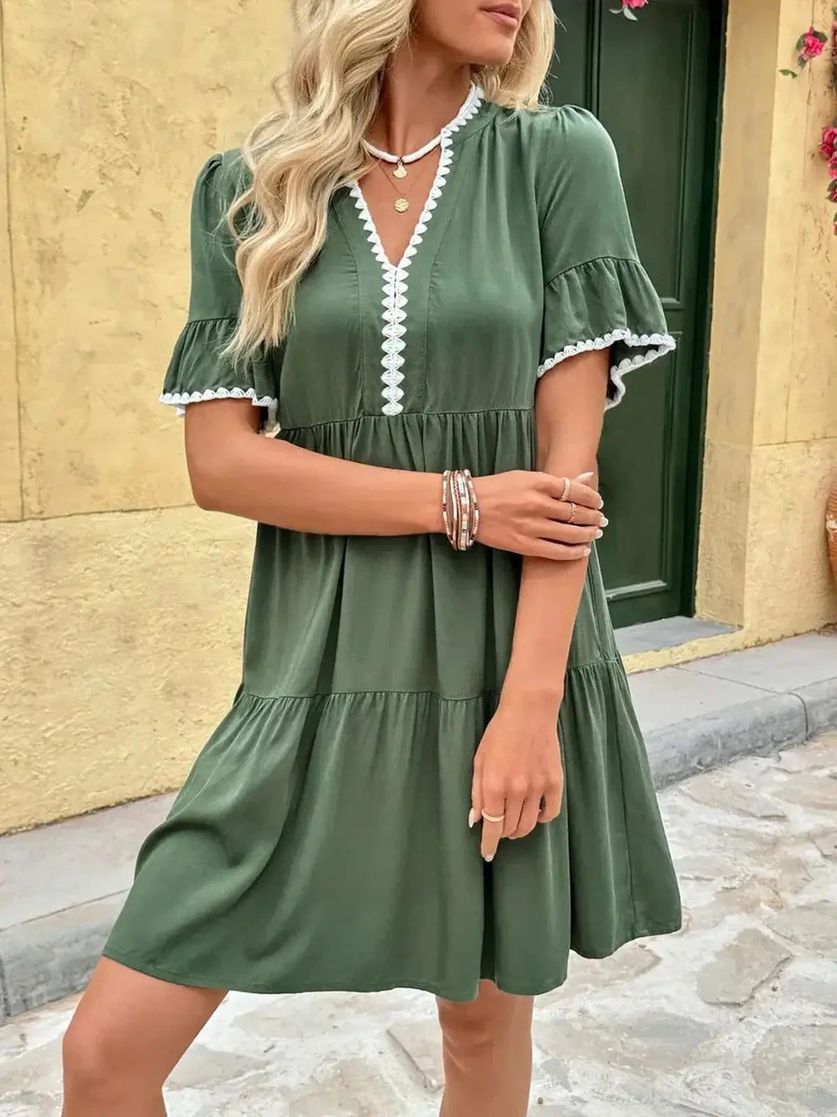 Model wearing a green Veranda Bloom Mini Dress with a V-neckline and white embroidered trim, perfect for summer occasions.