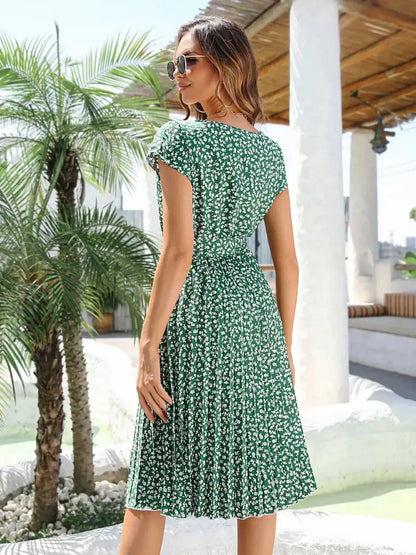 Woman wearing a green floral midi dress with pleats, short flutter sleeves, and cinched waist, perfect for summer occasions.