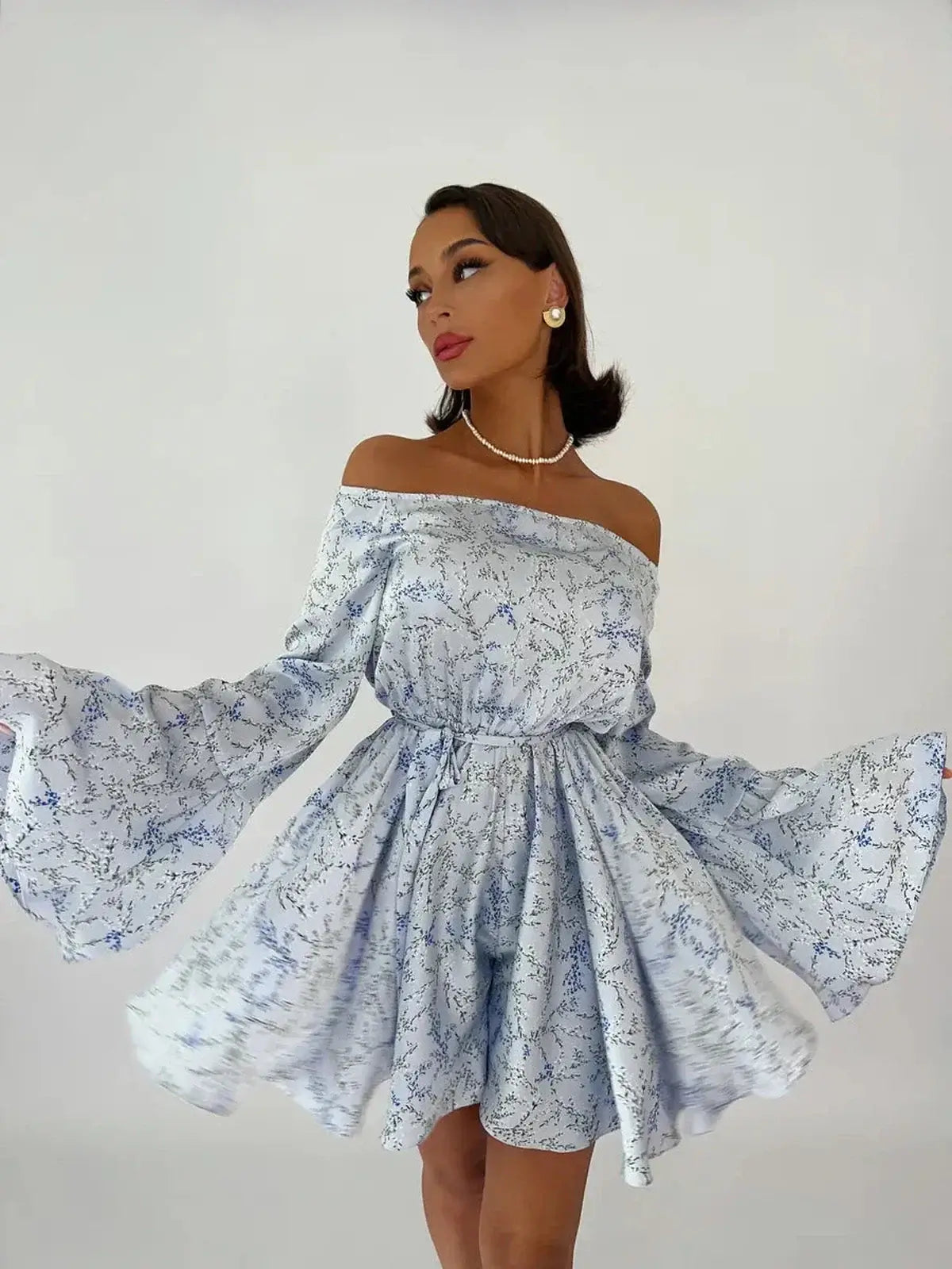 Model wearing Whimsy Flair Mini Dress with off-shoulder neckline and flowy bell sleeves, perfect for summer events.